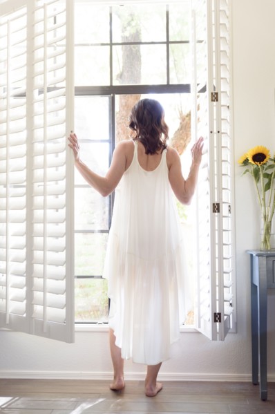 Caucasian woman wearing nightgown opening window shutters