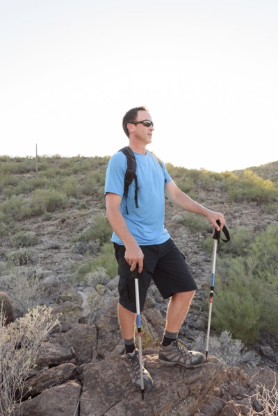 Hispanic hiker holding walking sticks on hill