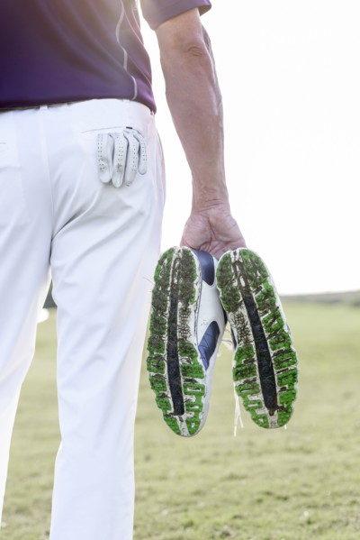 Hispanic man hold golf shoes covered with grass