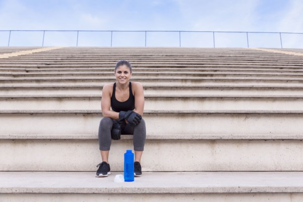 Hispanic woman wearing boxing gloves resting on bleachers
