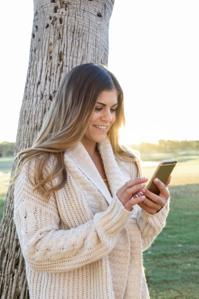 Hispanic woman leaning on tree texting on cell phone