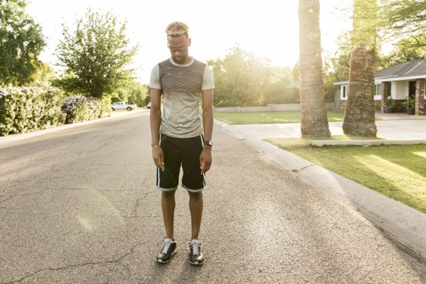 Black man standing on street in the neighborhood looking down