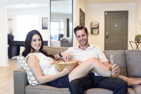 Smiling Caucasian couple relaxing on sofa with beer and popcorn