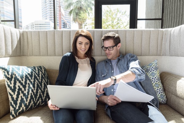 Caucasian couple on sofa holding laptop and paperwork