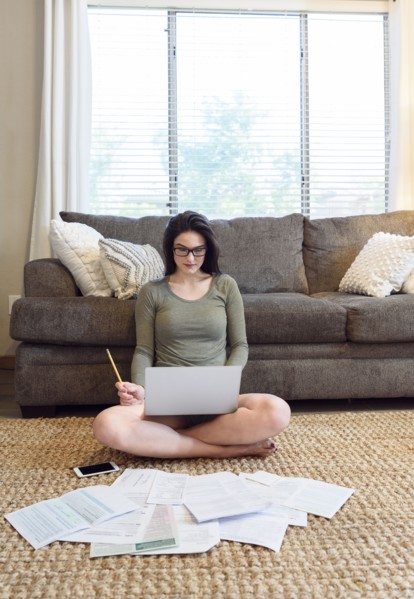 Caucasian woman sitting on floor using laptop near paperwork