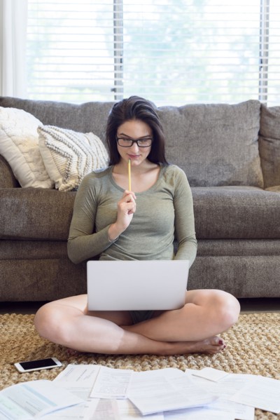 Caucasian woman sitting on floor using laptop near paperwork