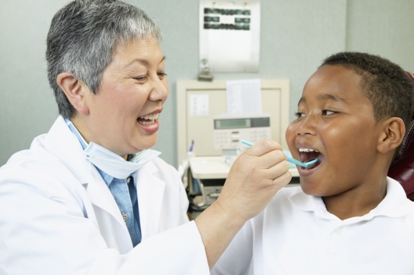 Senior Asian female dentist examining young male patient