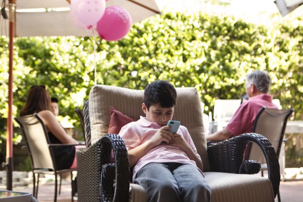 Bored boy using cell phone at party