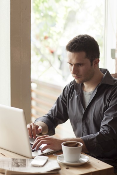 Man using laptop with cup of coffee in cafe