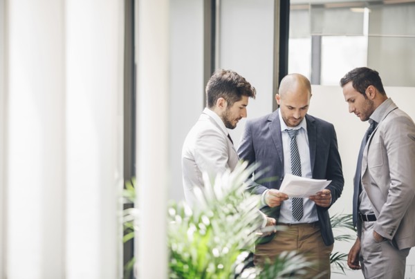 Caucasian businessmen reading paperwork in office corridor