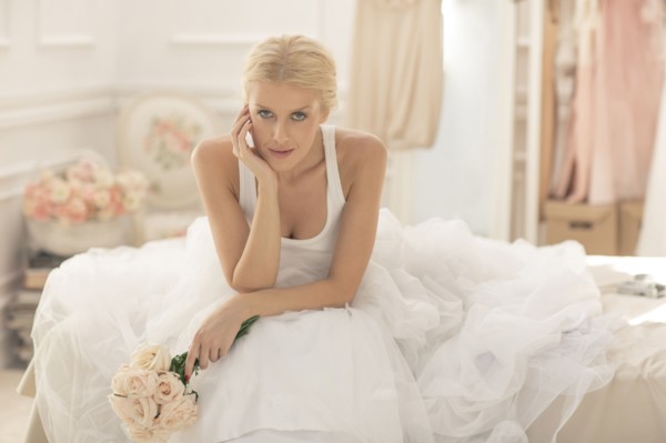Serious bride sitting with bouquet on bed
