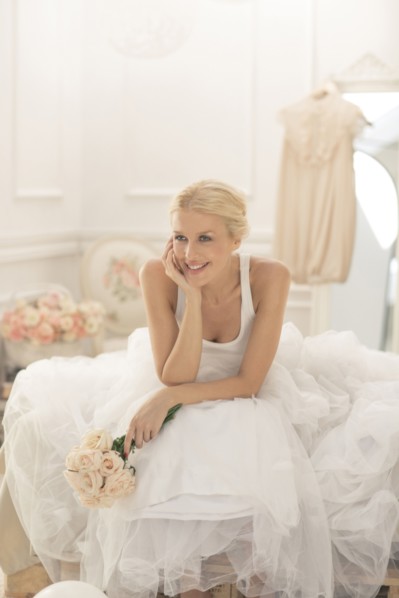 Smiling bride sitting with bouquet on bed