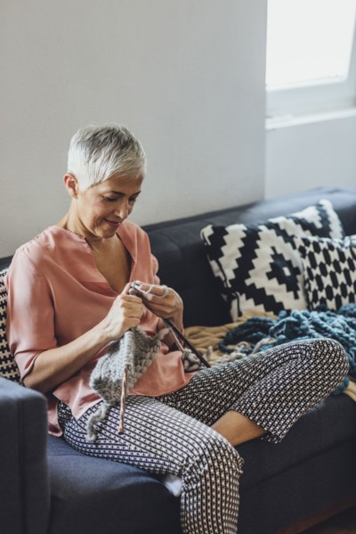 Older Caucasian woman knitting on sofa