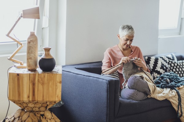 Older Caucasian woman knitting on sofa