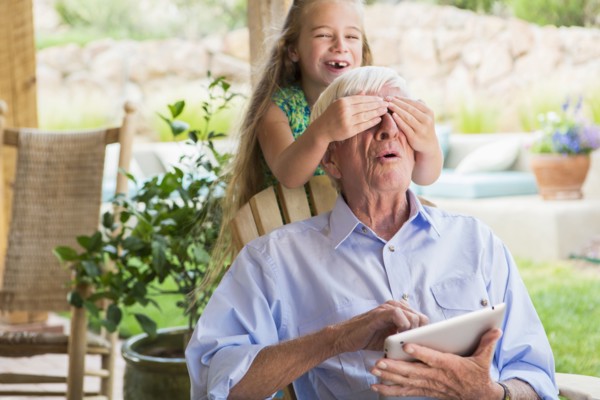 Caucasian girl covering grandfather's eyes on patio