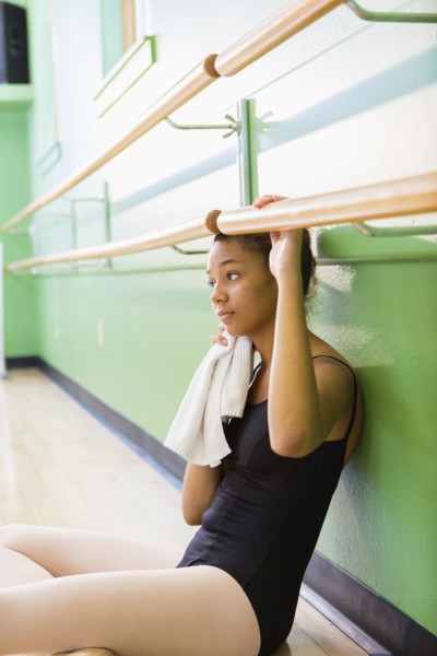 Mixed race ballerina sitting below barre