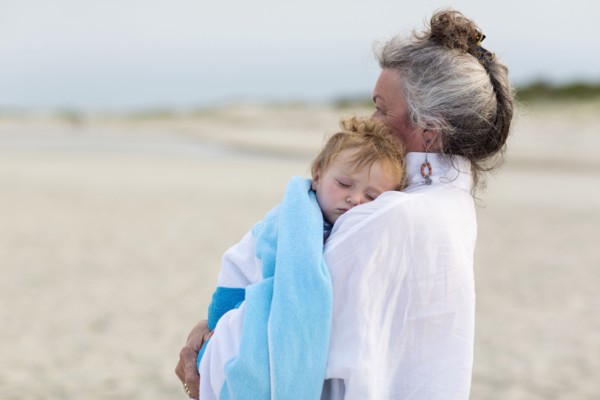 Caucasian woman carrying grandson on beach
