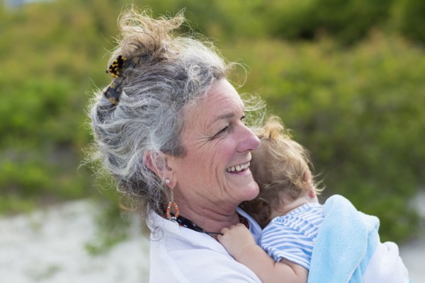 Caucasian woman carrying grandson on beach