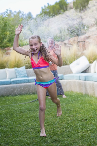 Caucasian grandmother spraying granddaughter with water in backyard