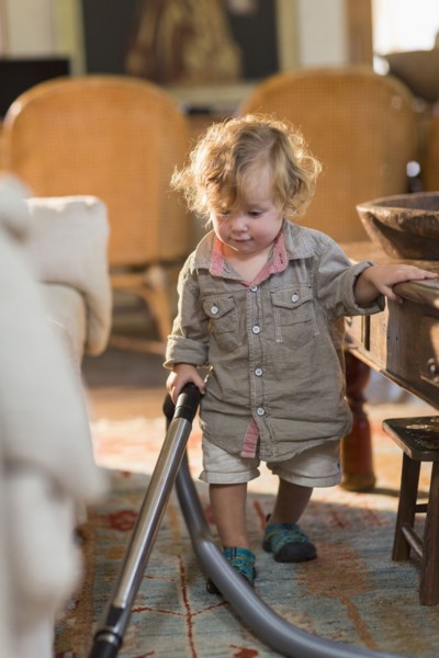 Caucasian baby boy vacuuming living room rug