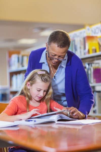 Teacher helping student use digital tablet in library