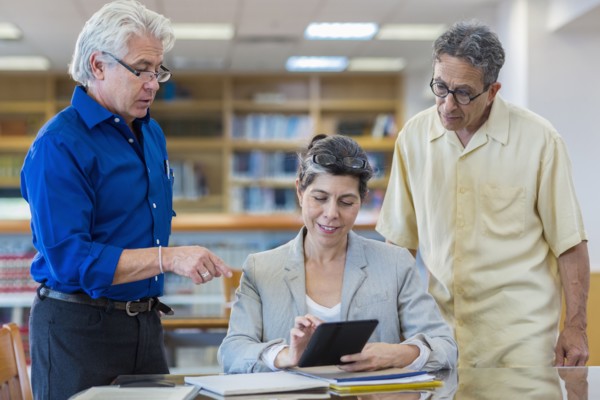 Teacher helping adult students use digital tablet in library