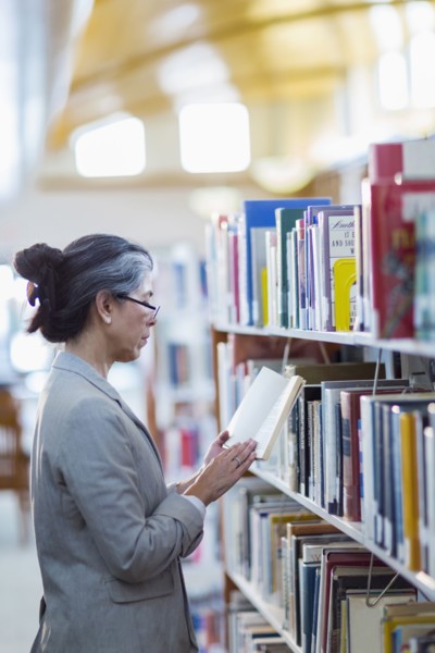 Older Hispanic woman reading book in library