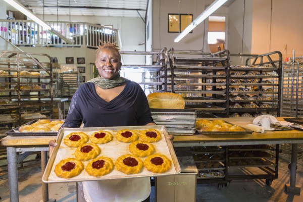 Black baker holding tray of pastries in bakery kitchen