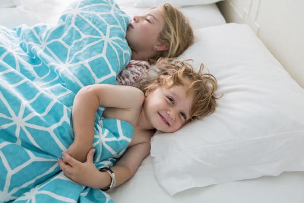 Caucasian brother and sister laying in bed
