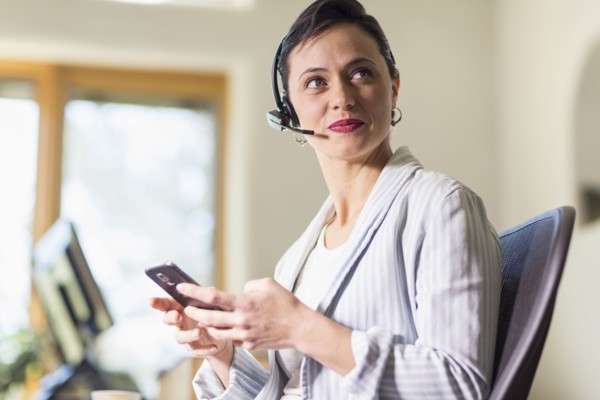 Businesswoman using cell phone and headset in office