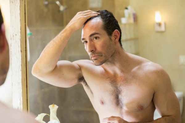 Hispanic man checking receding hairline in mirror