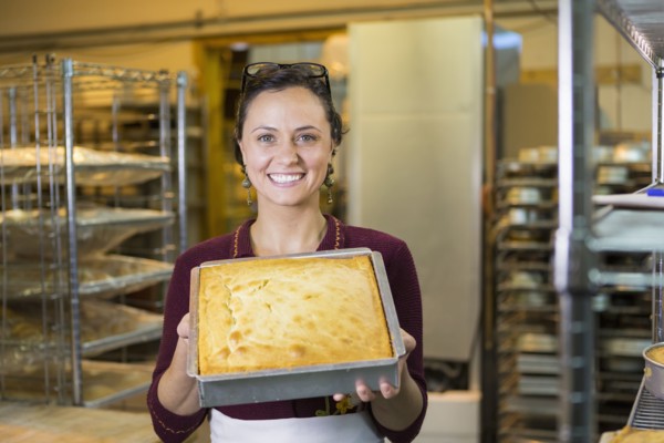 Caucasian woman showing cake in bakery pan
