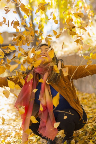 Smiling Asian woman throwing leaves in autumn