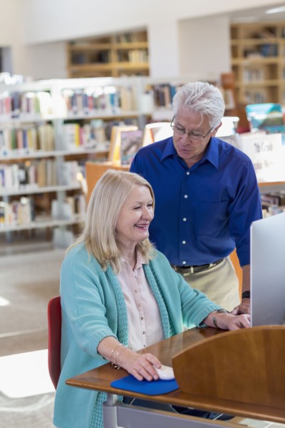 Older man watching woman using computer in library