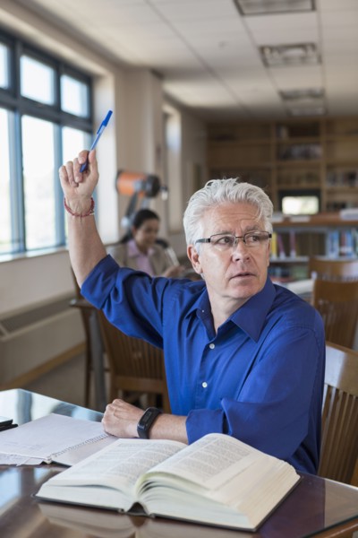 Older man in library raising hand and asking question