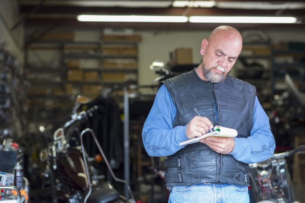 Caucasian man near motorcycle writing on notepad