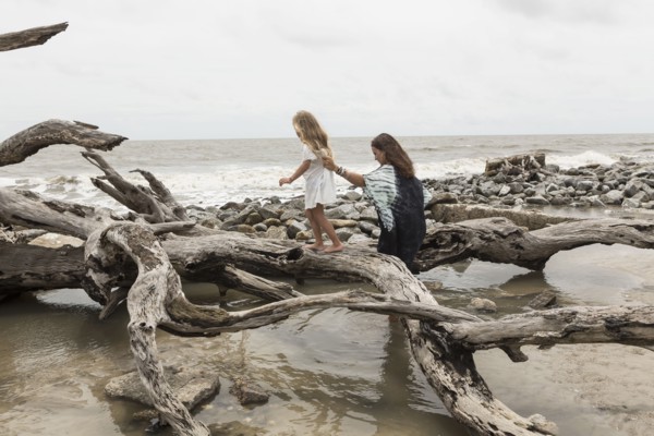 Caucasian mother and daughter walking on driftwood on beach