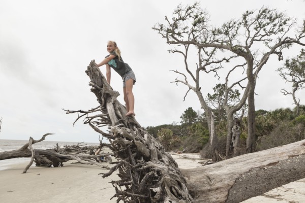 Caucasian girl climbing on driftwood on beach