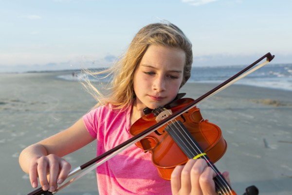 Caucasian girl playing violin on windy beach