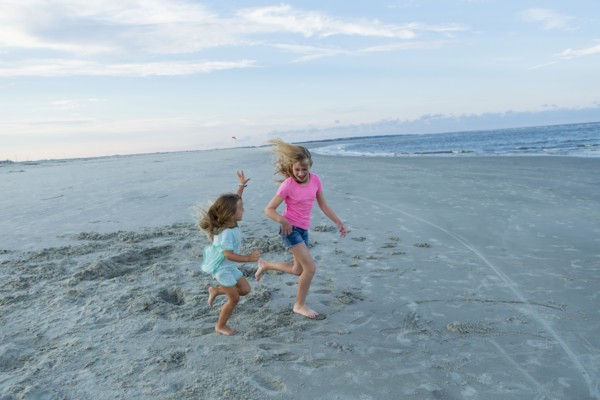 Caucasian sisters running on windy beach