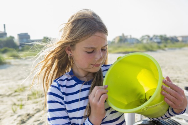 Caucasian girl holding crab in bucket on windy beach