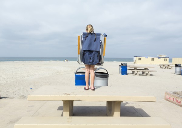 Caucasian girl carrying folding chair on picnic table at beach