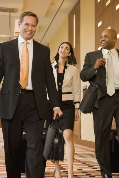 Multi-ethnic business people walking with suitcases down corridor