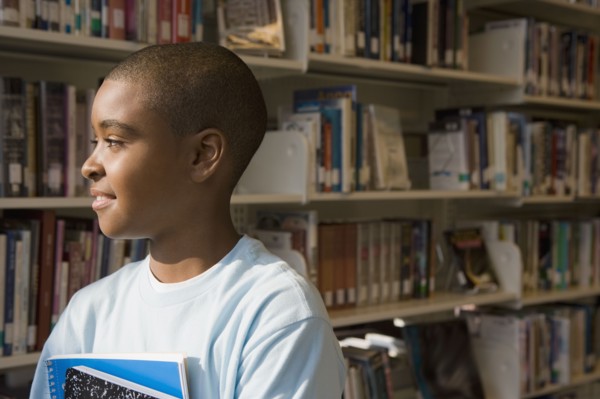 Mixed race boy holding books in library