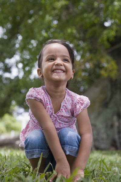Grinning Hispanic preschool girl squatting in grass
