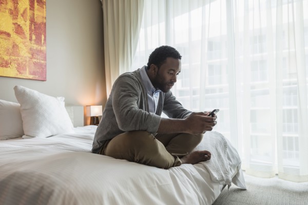 Black man using cell phone on bed