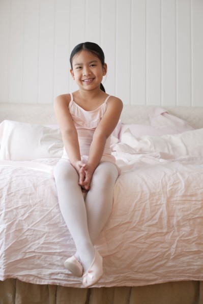 Asian girl in ballet costume sitting on bed