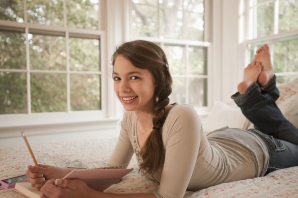 Mixed race girl laying in bed writing in journal