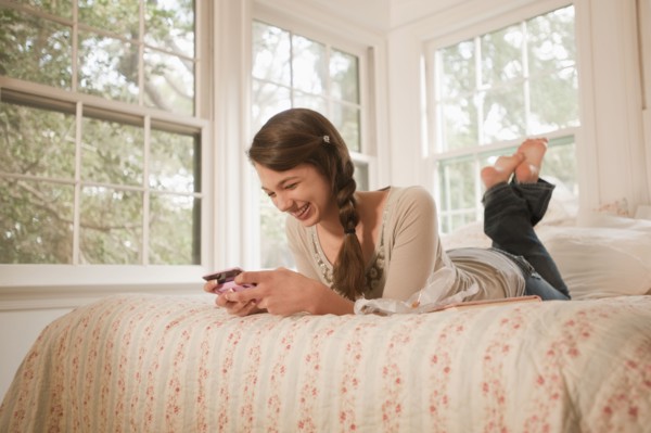 Mixed race girl laying in bed text messaging on cell phone
