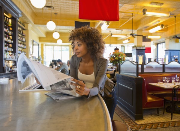 African American woman reading newspaper in cafe